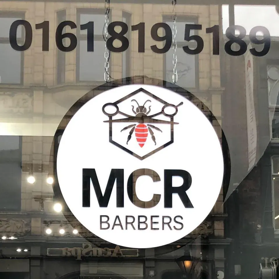 The MCR Barbers sign and the shop's phone number, 0161 819 5189, in the front window