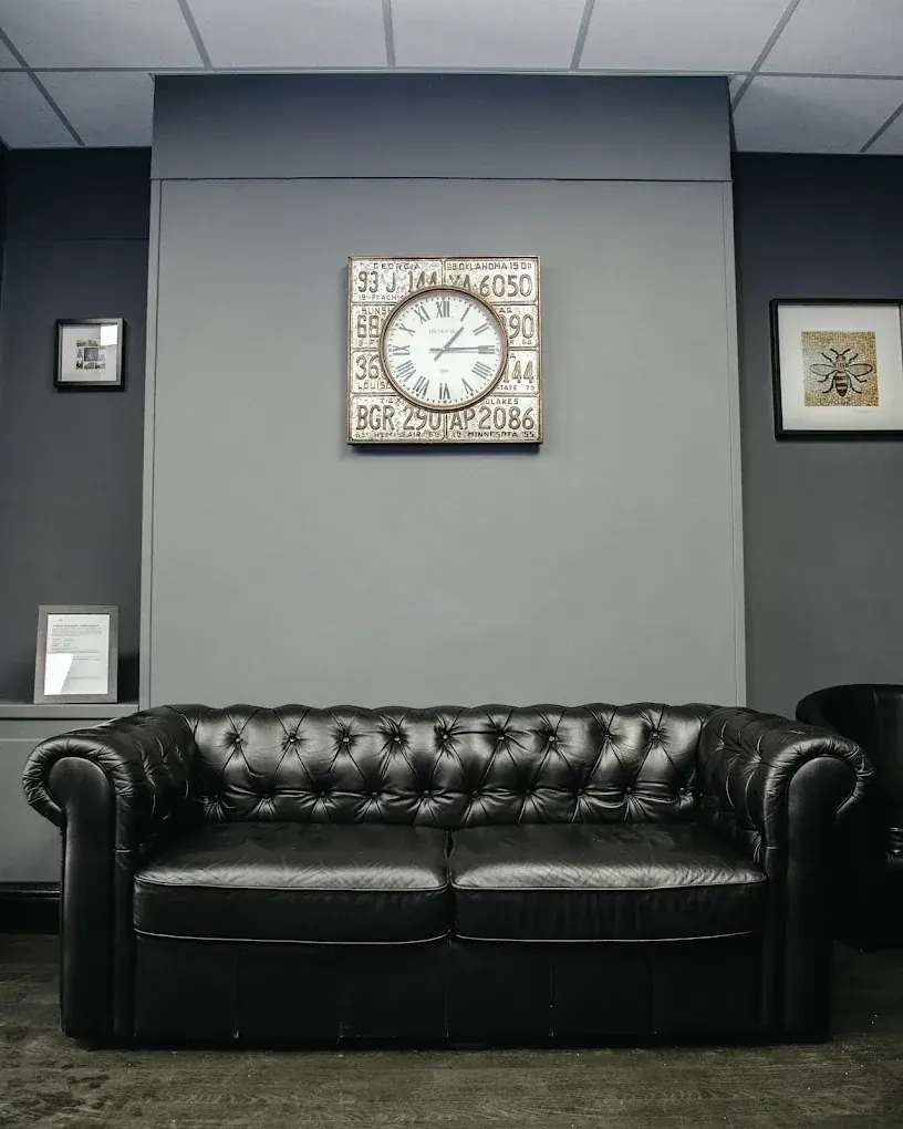 The waiting area: a black leather Chesterfield sofa under a number-plate clock and a Manchester bee print