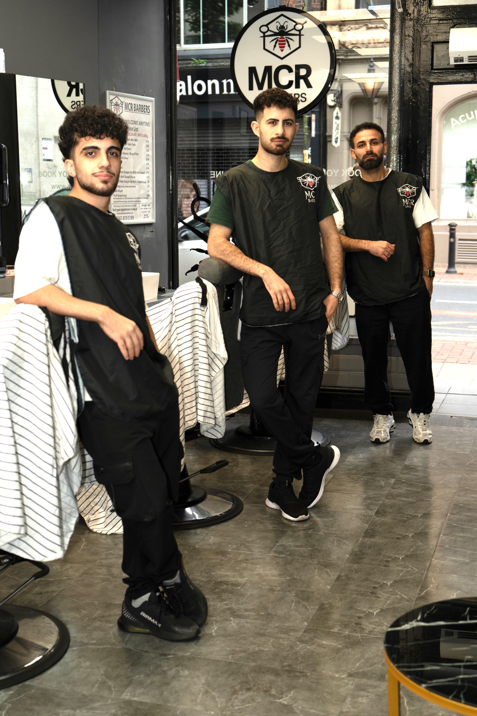 Barbers at work on the shop floor at Manchester Barbers, with the front window behind them